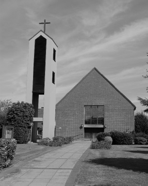**Alt-Text:** Schwarz-weiß-Foto einer modernen Backsteinkirche mit Satteldach und freistehendem, schlankem Glockenturm mit Kreuz, zu der ein gepflasterter Weg zwischen Rasenflächen und Hecken führt.**Hinweise zur Verwendung:**
- Ich sehe nur dieses eine Bild. Wenn du weitere Bilder hast, schick sie mir gern, dann erstelle ich für jedes einen eigenen Alt-Text.
- Mir ist nicht bekannt, welche Kirche das ist und wo sie steht. Falls das Bild auf der Webseite der „Platt AG der Grafschaft Bentheim“ einen konkreten Bezug hat, etwa zu plattdeutschen Gottesdiensten oder einer Veranstaltung in dieser Kirche, kann ich den Alt-Text anpassen. Zum Beispiel: „Die evangelisch-reformierte Kirche in …, in der regelmäßig plattdeutsche Gottesdienste stattfinden, …“ Dafür bräuchte ich den Namen der Kirche und den Zusammenhang.