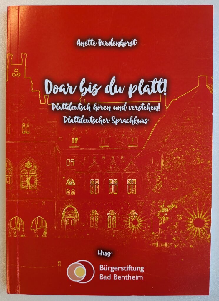 Buchcover von „Doar bis du platt! – Plattdeutsch hören und verstehen! Plattdeutscher Sprachkurs“ von Anette Bardenhorst, herausgegeben von der Bürgerstiftung Bad Bentheim, mit weißer Schrift auf rotem Hintergrund und einer gelb umrissenen Zeichnung eines historischen Gebäudes mit Türmen, Spitzbogenfenstern und Bäumen.