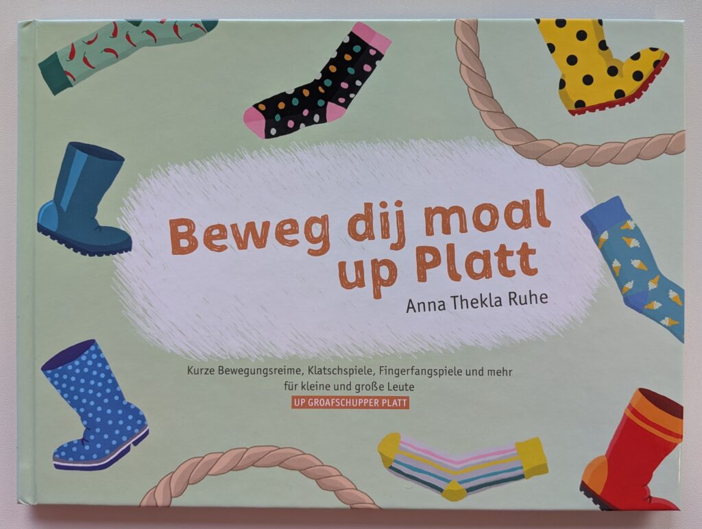 Buchcover von „Beweg dij moal up Platt“ von Anna Thekla Ruhe mit bunten Socken, Gummistiefeln und Seilen auf hellgrünem Hintergrund, Untertitel: Kurze Bewegungsreime, Klatschspiele, Fingerfangspiele und mehr für kleine und große Leute up Groafschupper Platt.