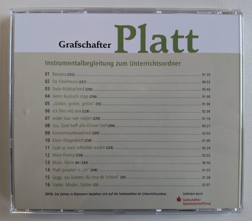 Rückseite der CD-Hülle „Grafschafter Platt – Instrumentalbegleitung zum Unterrichtsordner“ mit einer Liste von 16 plattdeutschen Liedern samt Spielzeiten und Seitenverweisen, gefördert durch die Grafschafter Sparkassenstiftung.