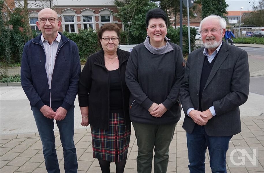 Vier Personen der Platt AG der Grafschaft Bentheim – zwei Männer und zwei Frauen in Alltagskleidung – stehen nebeneinander auf einem gepflasterten Gehweg vor einem Backsteingebäude und Bäumen und lächeln in die Kamera.